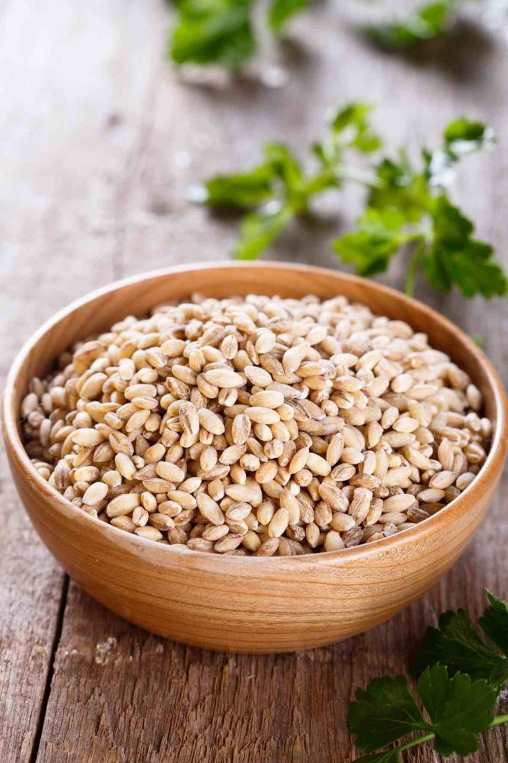 a wooden bowl filled with seeds and parsley on top of a wooden table next to leaves