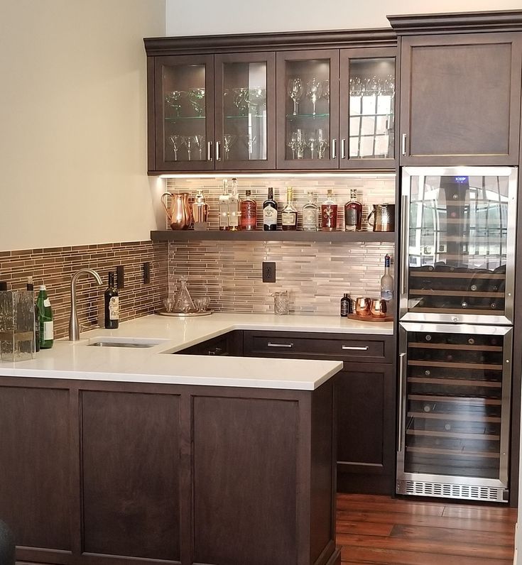 a kitchen with brown cabinets and white counter tops is pictured in this image, there are wine bottles on the shelves