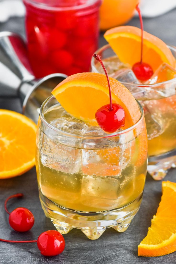 two glasses filled with liquid and garnished with orange slices, cherries and cherry