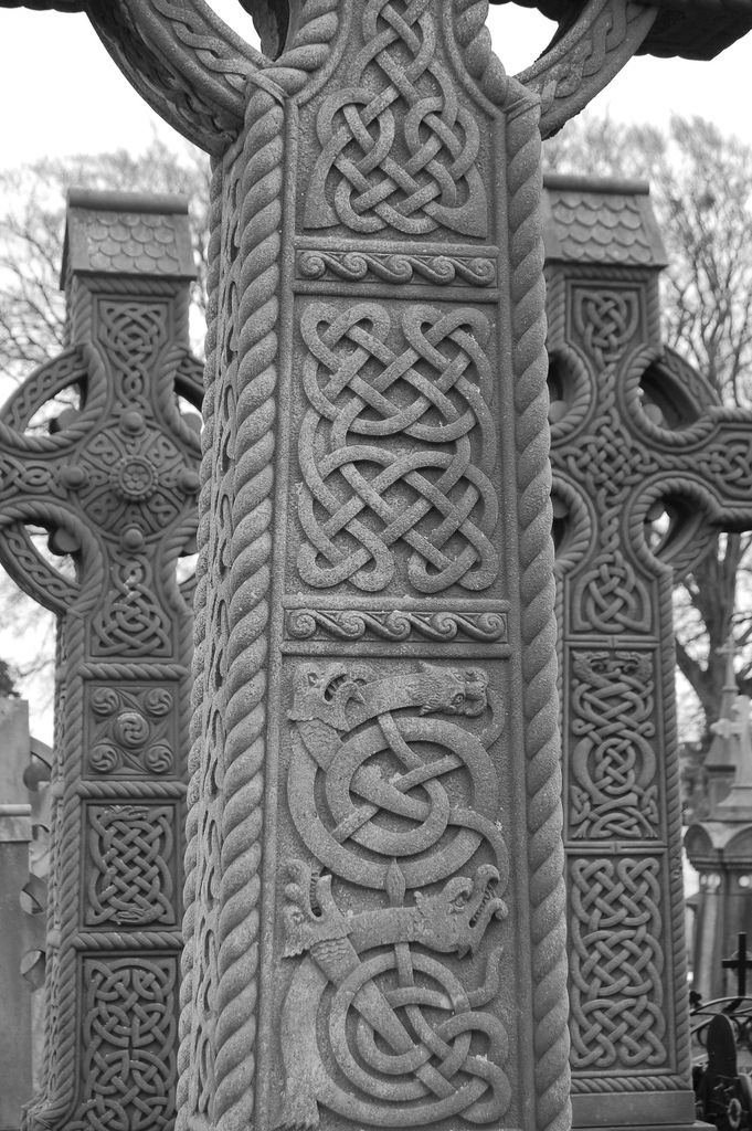 an intricately carved pillar in the middle of a cemetery with crosses and headstones