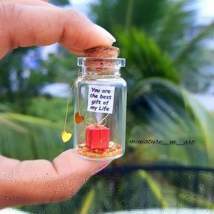 a hand holding a tiny glass jar filled with lots of gold coins and a message on it