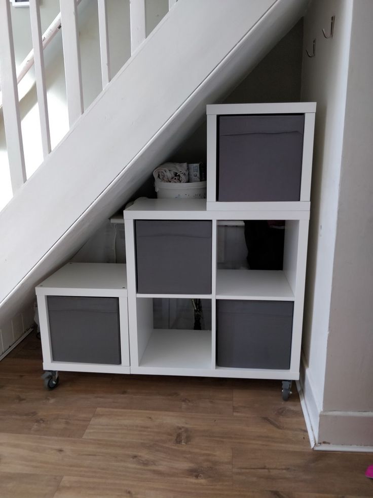 an under the stairs storage unit with grey drawers and white shelves below it, underneath a stair case