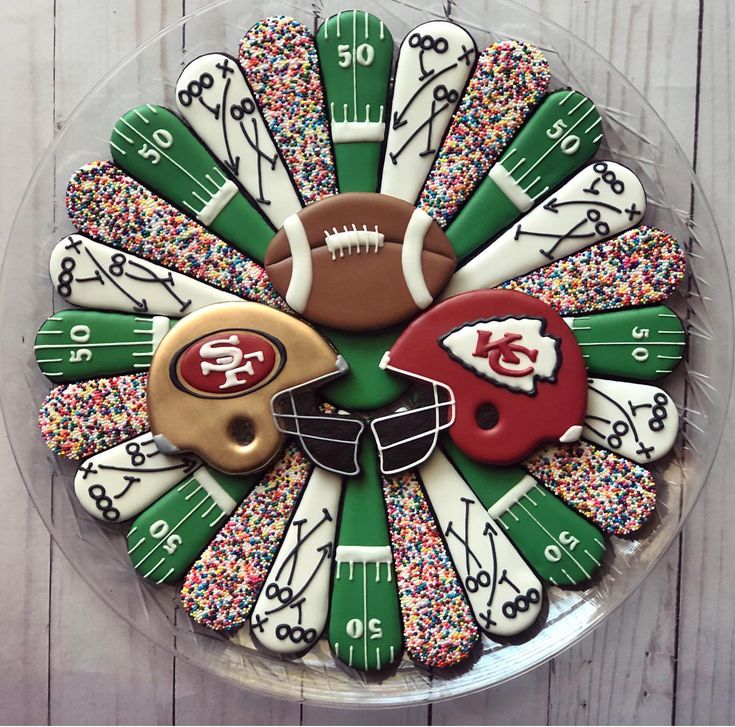 decorated cookies in the shape of footballs and helmets on a platter with sprinkles