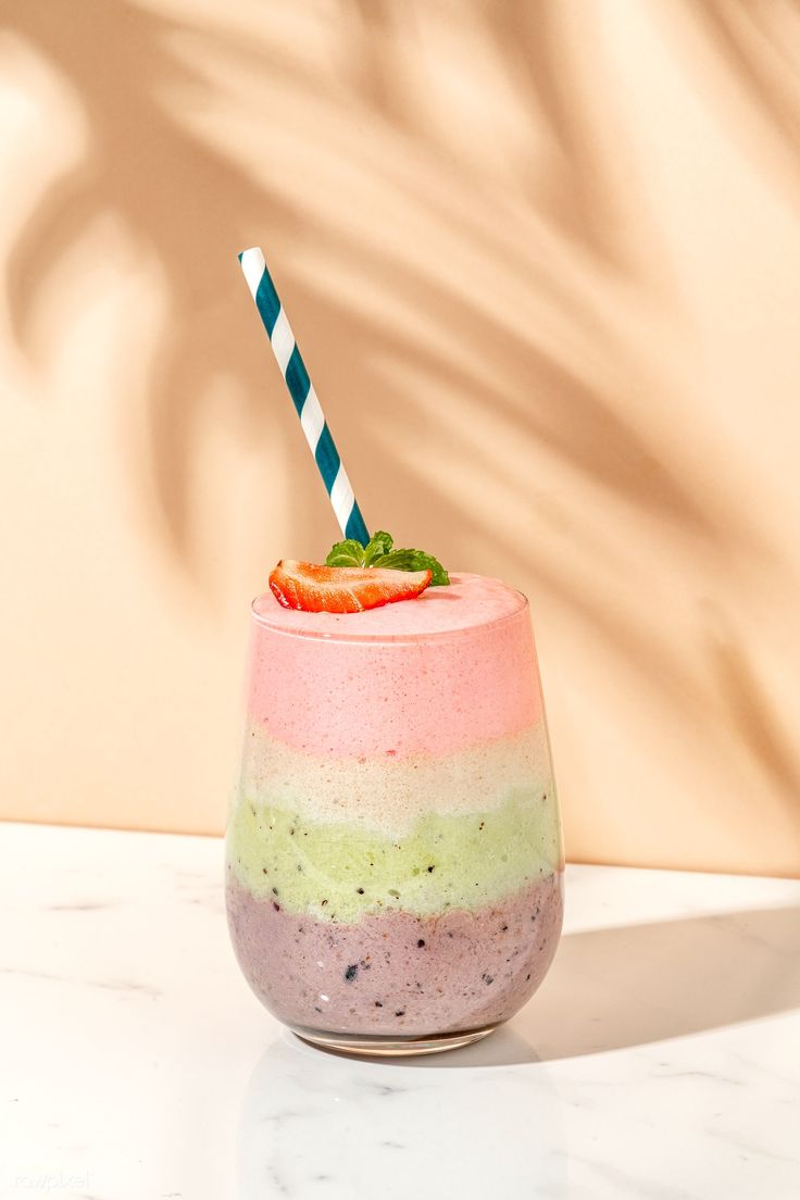 a smoothie in a glass with a striped straw on the top and a green, pink, blue, and white stripe