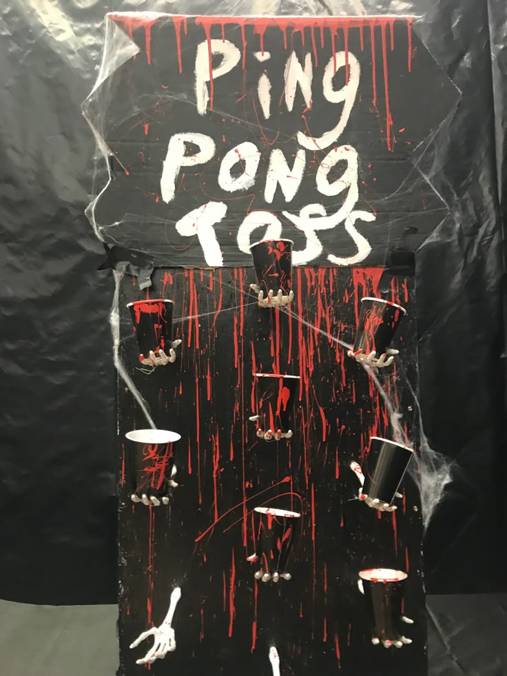 a sign that says ping pong toss in front of a black background with red and white paint splattered on it