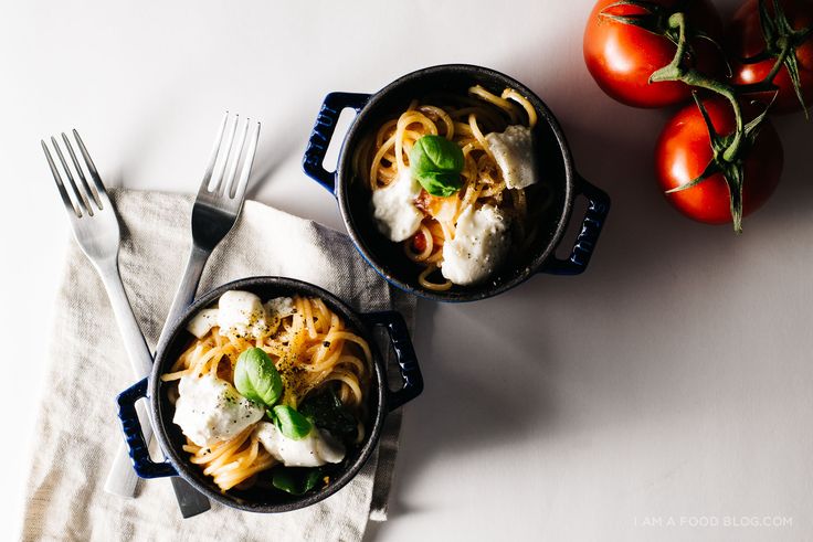 two pans filled with pasta and tomatoes on top of a white table next to each other