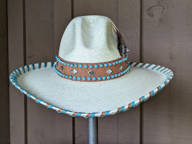 This pretty hat Faith, starts with the popular and very flattering palm Gus hat body. It has a 4" brim and a 5 1/4" crown. The hatband is designed with saddle colored leather that has been decorated with two rows of faux turquoise spots and a row of diamond spots. The brim is hand laced in saddle and turquoise. Finished with a complementing feather. Note: All hats are made to order. Please up to 4 weeks for your hat to ship. Artisan Turquoise Hats For Western-themed Events, Artisan Turquoise Hat For Western-themed Events, Southwestern Turquoise Hat Band For Ranch, Southwestern Turquoise Hat Bands For Country Events, Artisan Turquoise Hat With Curved Brim, Artisan Turquoise Curved Brim Hat, Western Handmade Panama Hat For Kentucky Derby, Turquoise Hat For Kentucky Derby, Turquoise Hats For Country Events With Short Brim