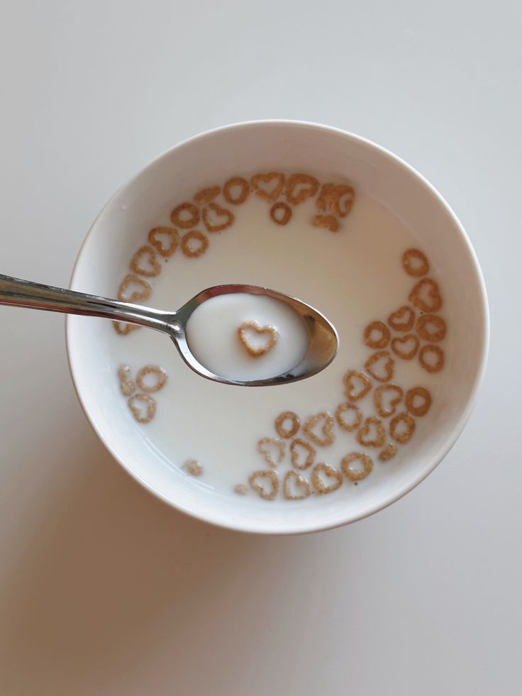 a spoon in a bowl filled with cereal and heart - shaped candies on the side