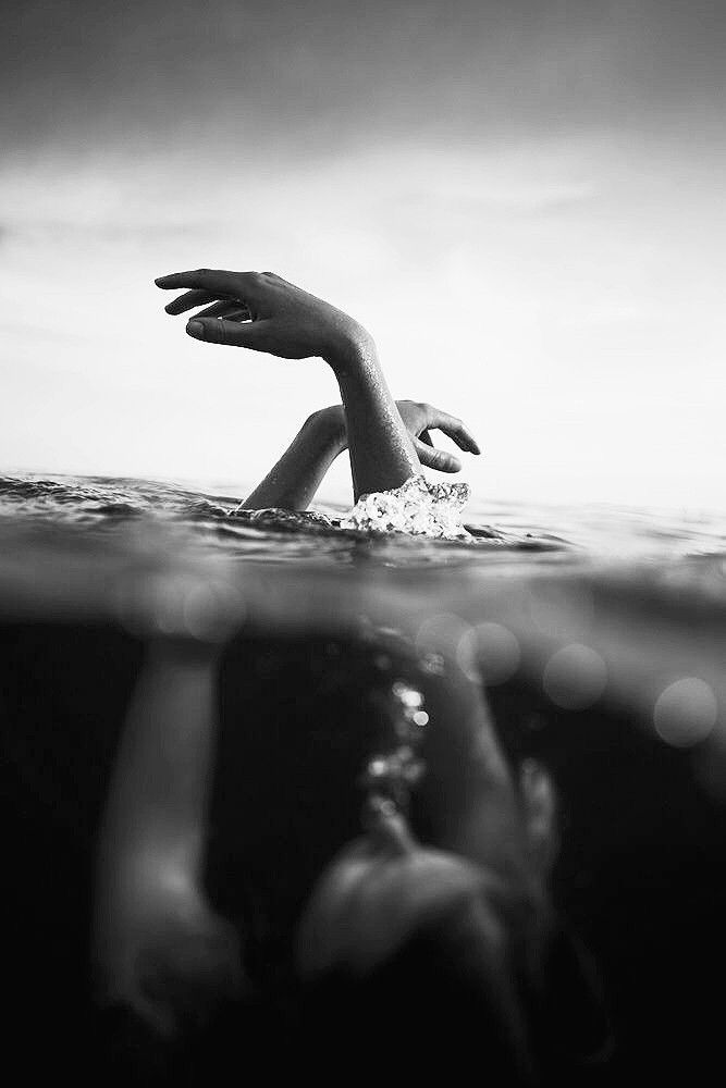 a person swimming in the ocean with their hand up to the water's surface