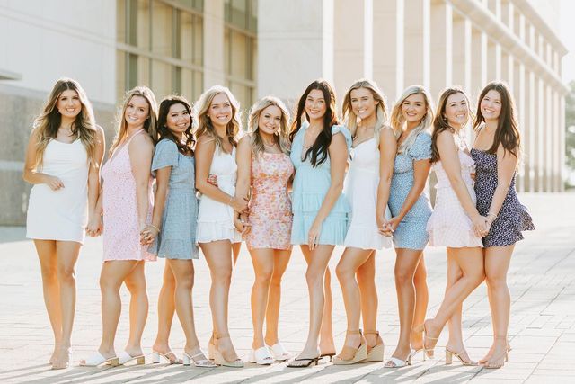 a group of young women standing next to each other in dresses and sandals on the sidewalk