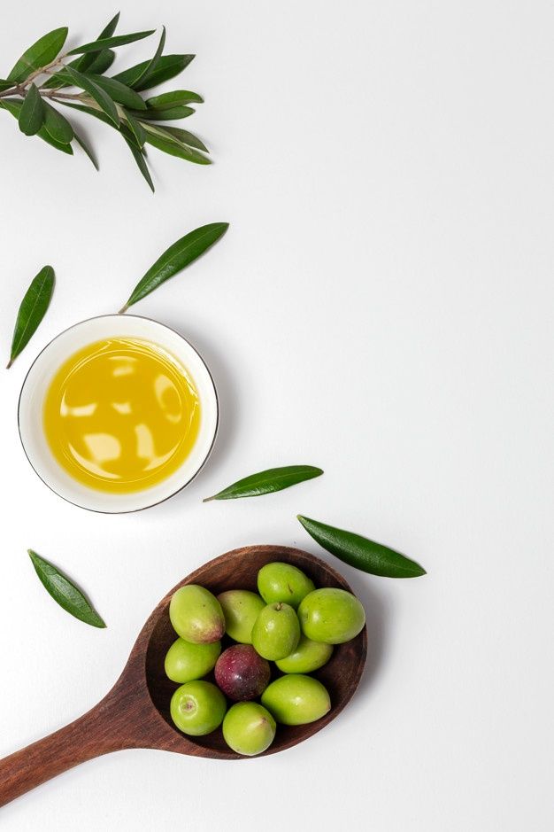 olives in a wooden spoon next to an olive oil bottle on a white surface