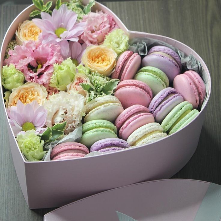 a heart shaped box filled with macaroons and flowers on top of a table