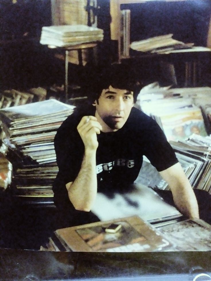 a man sitting at a table in front of stacks of books and magazines with his hand on his chin