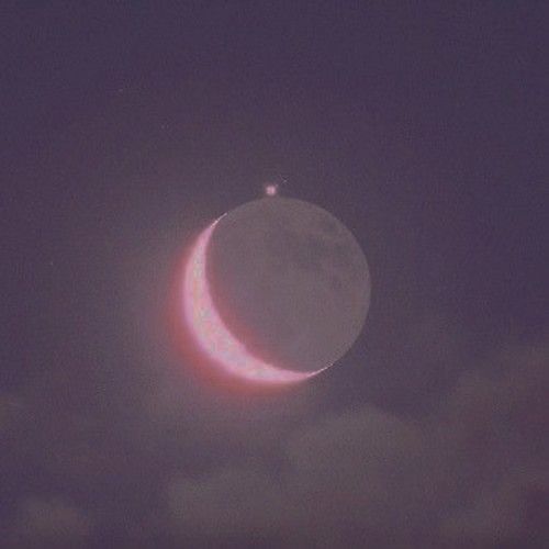 the moon is seen in front of a dark night sky with clouds and pink hues