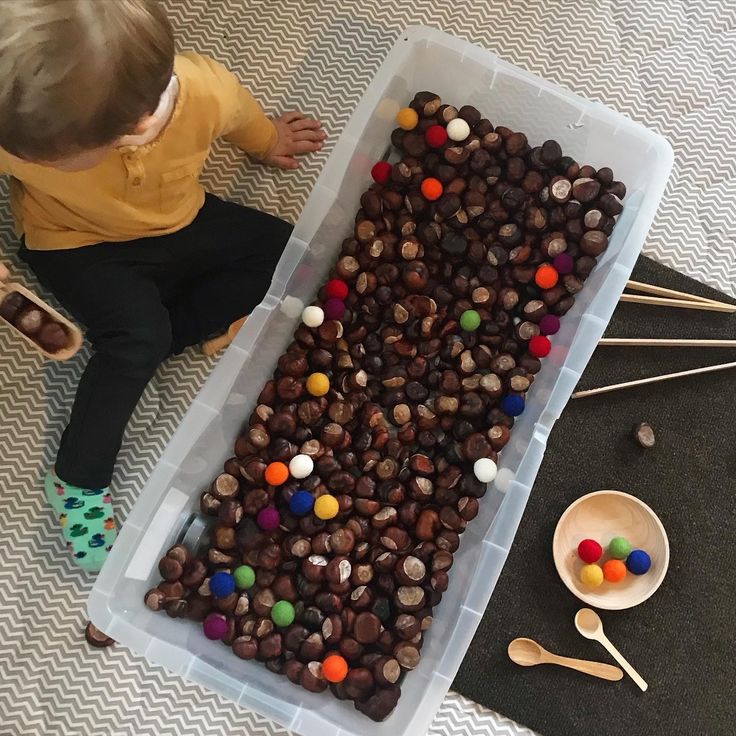 a toddler sitting on the floor next to a plastic container filled with chocolate candies