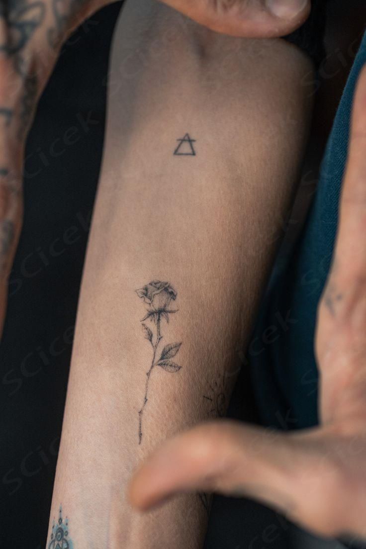 a person with a tattoo on their arm holding a flower in one hand and an arrow in the other