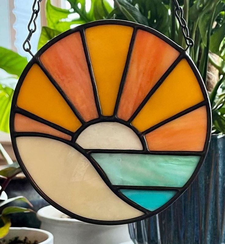 a stained glass sun catcher hanging from a chain in front of a potted plant