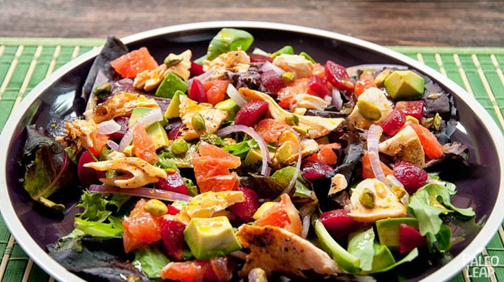 a salad with chicken, avocado and tomatoes on a purple plate sitting on a green place mat