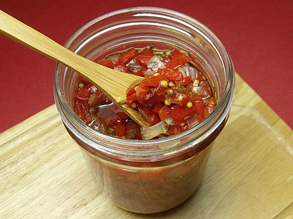 a wooden spoon in a glass jar filled with pickled tomatoes and corn kernels