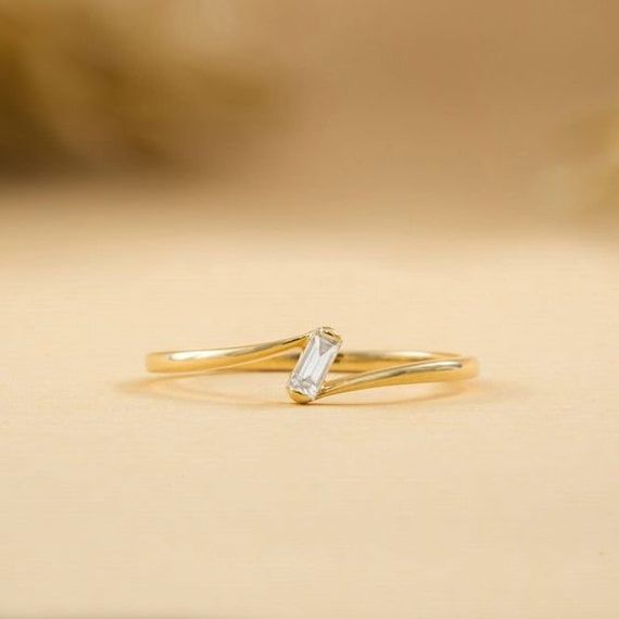 a gold ring with a white diamond on it sitting on a beige surface, in front of a blurry background