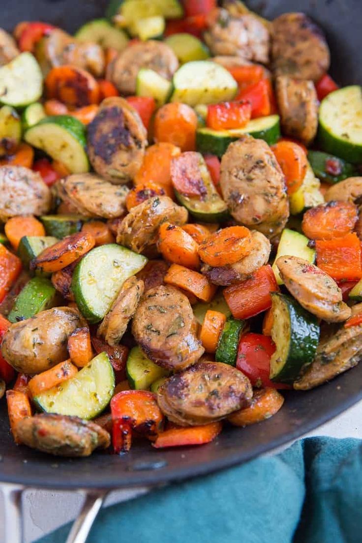 a skillet filled with sausage, zucchini, and vegetables on top of a blue towel