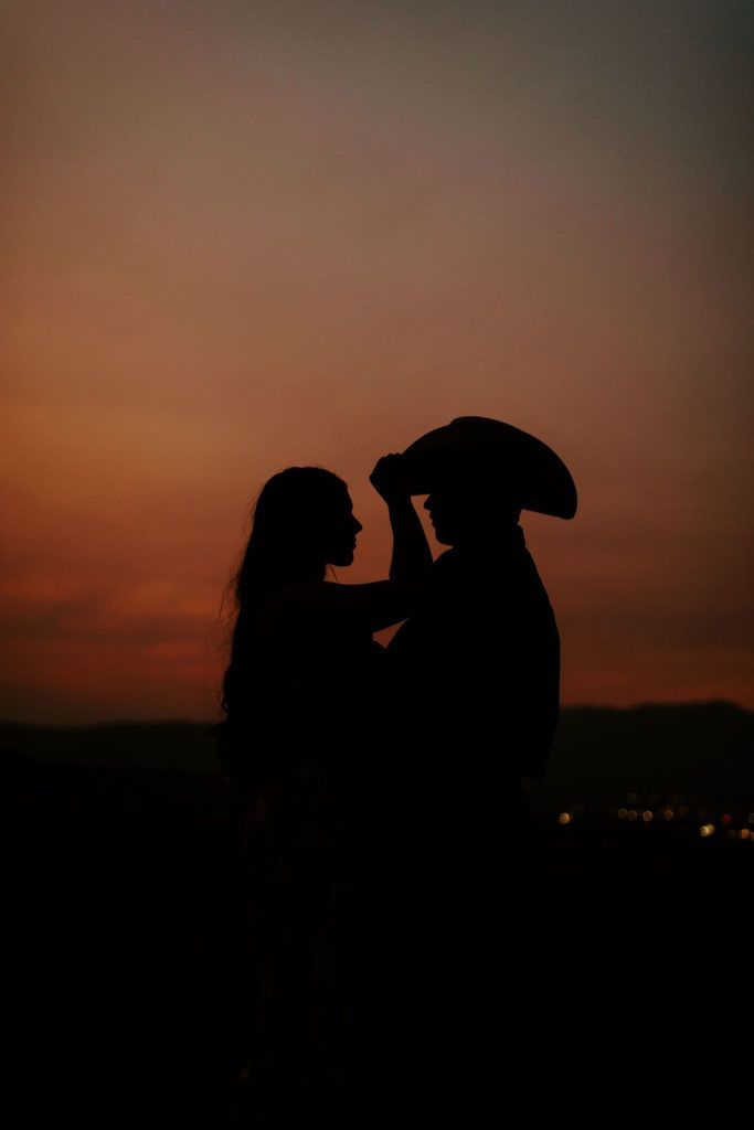 two people standing next to each other with an umbrella over their heads at sunset or dawn