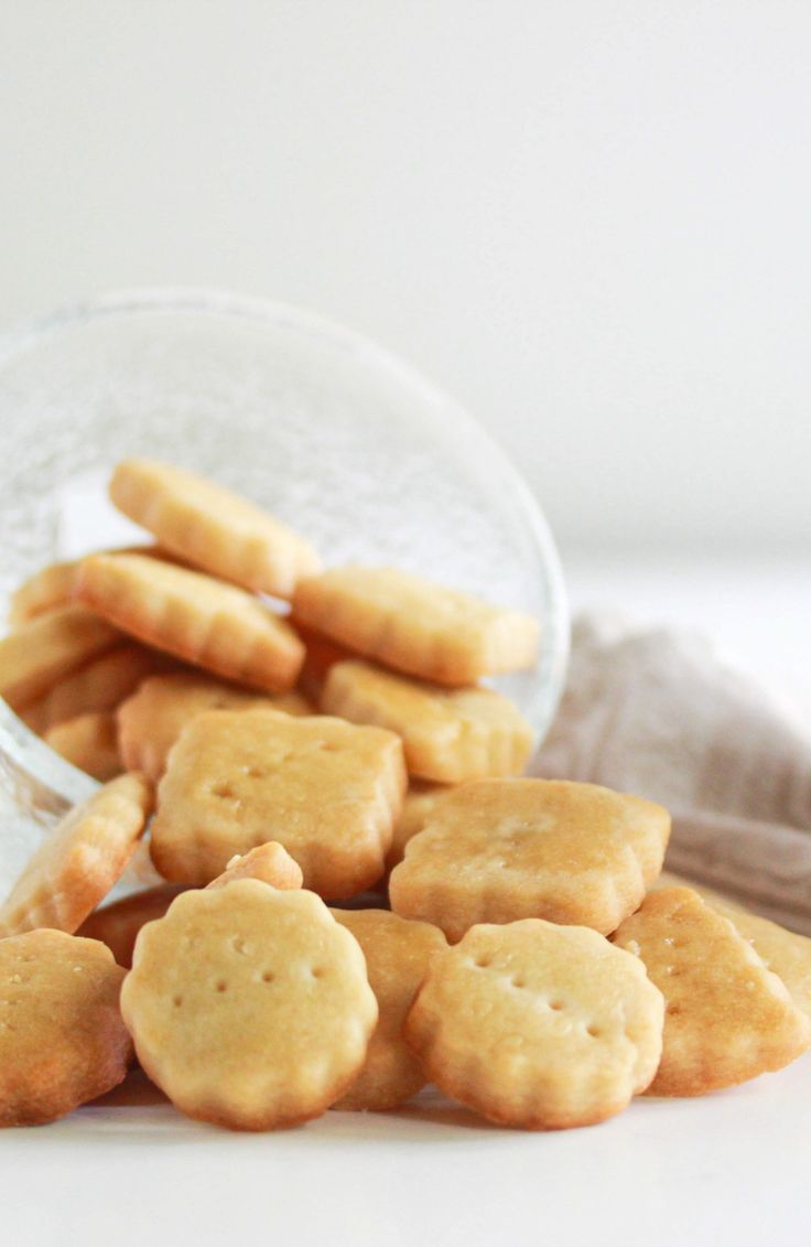 a glass bowl filled with short crackers on top of a white tablecloth next to a pile of cookies