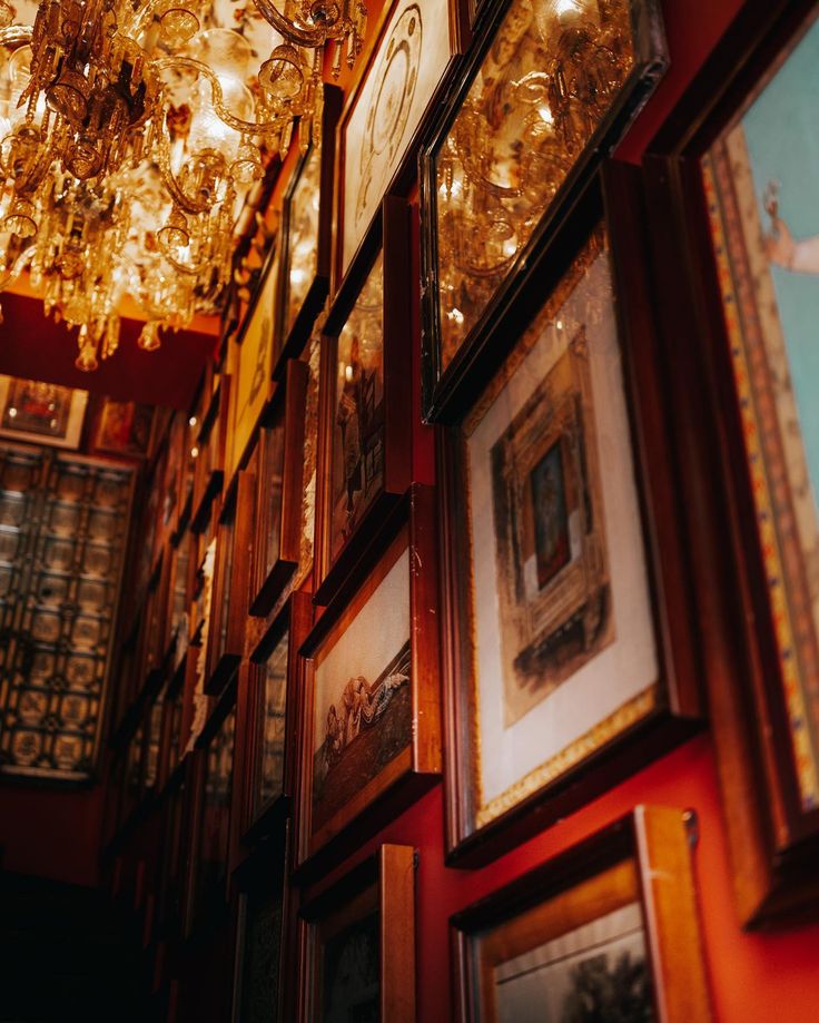 many framed pictures hang on the wall in a room with chandelier above them