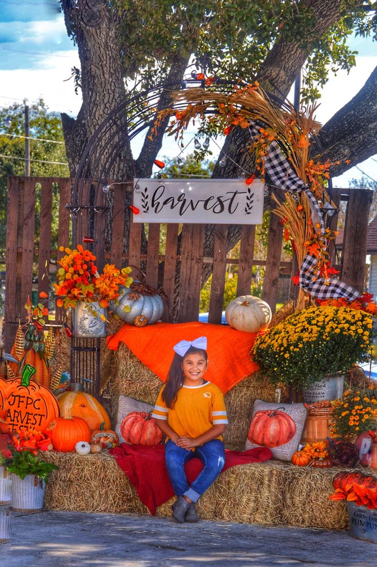 a woman sitting on hay bales with pumpkins