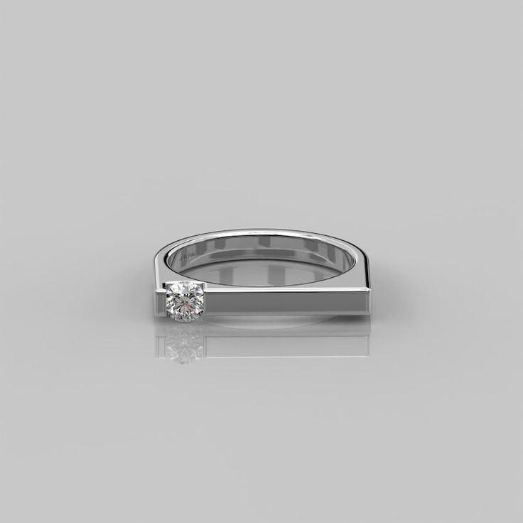 a white gold ring with a single diamond in the center on a reflective surface,