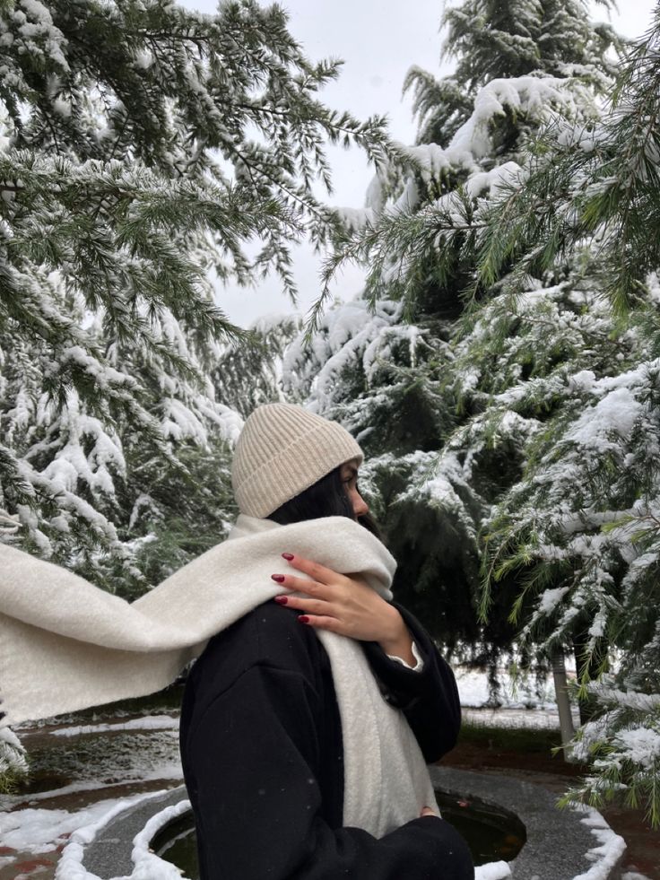 a woman is sitting in the snow with her arms wrapped around her neck and looking into the distance