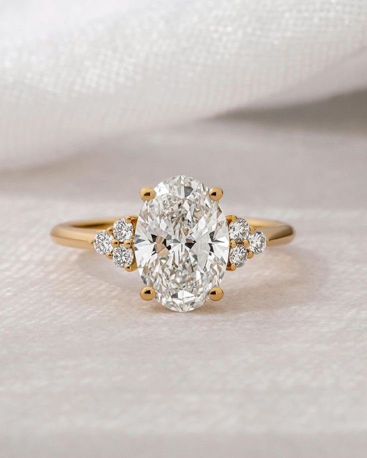 an oval cut diamond ring with three smaller round diamonds on the band, set in 18k yellow gold