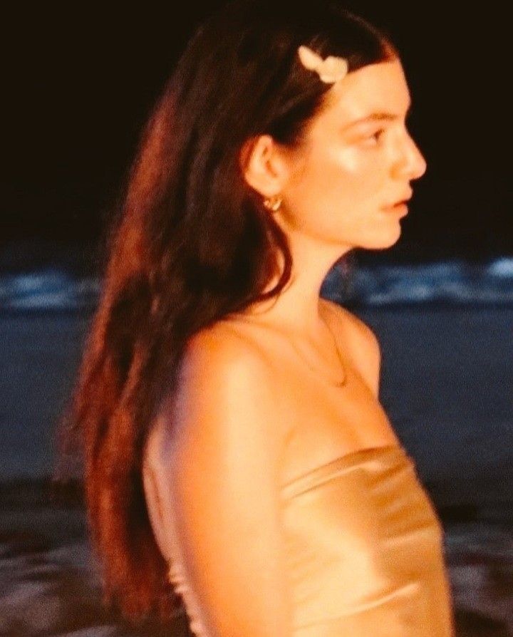 a woman with long hair standing in the water at night, wearing a gold dress