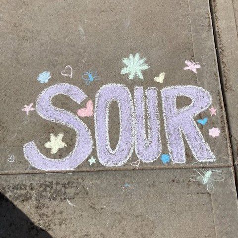 someone is standing on the sidewalk with their feet up in front of chalk writing that says sour