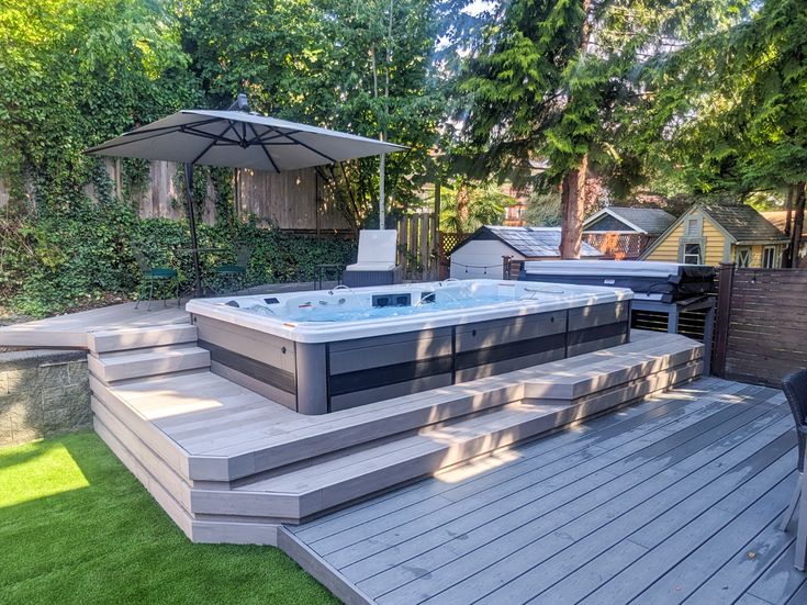 a hot tub sitting on top of a wooden deck next to a lush green yard