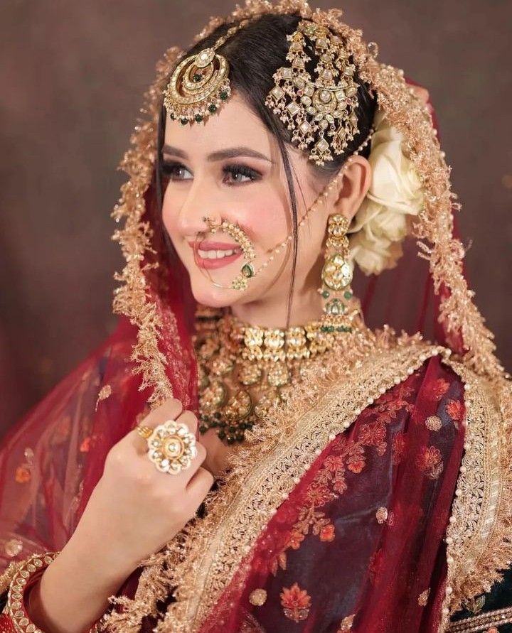 a woman in a red and gold bridal outfit with jewelry on her face, smiling at the camera