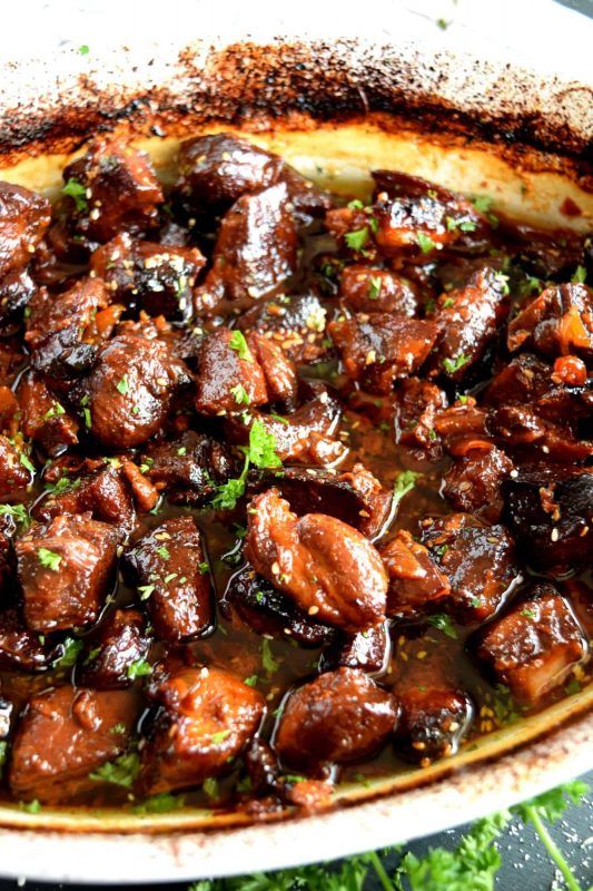 the dish has meat and sauce in it on the table next to some green leaves