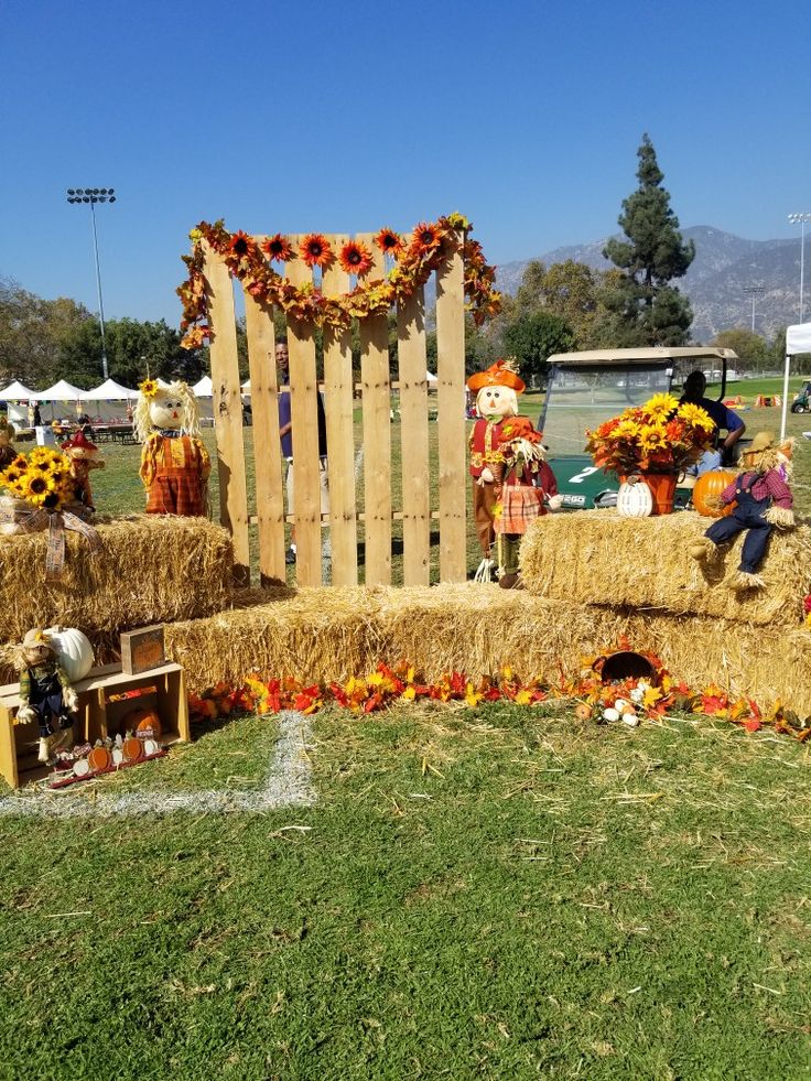 an outdoor display with hay bales and sunflowers on the grass, including scarecrows