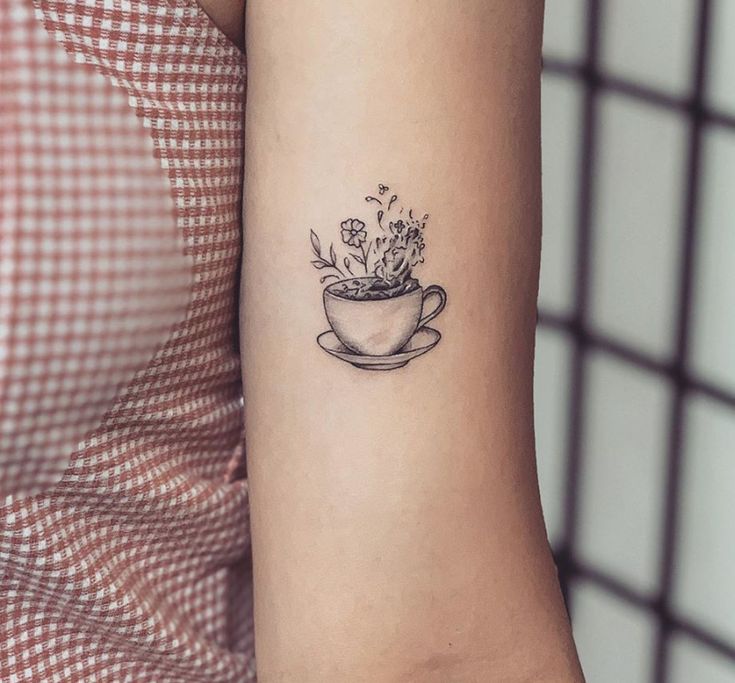 a small tattoo on the arm of a woman with a coffee cup and flowers in it