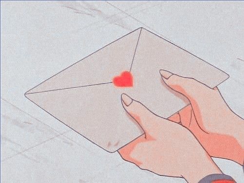 a person's hand holding an envelope with a red heart on it and the letter is in front of them