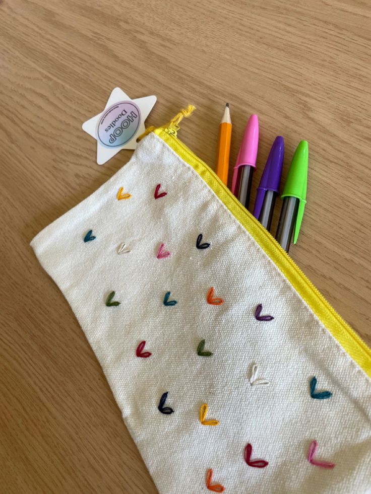 several colored markers are in a zippered pouch on a wooden table next to some pens