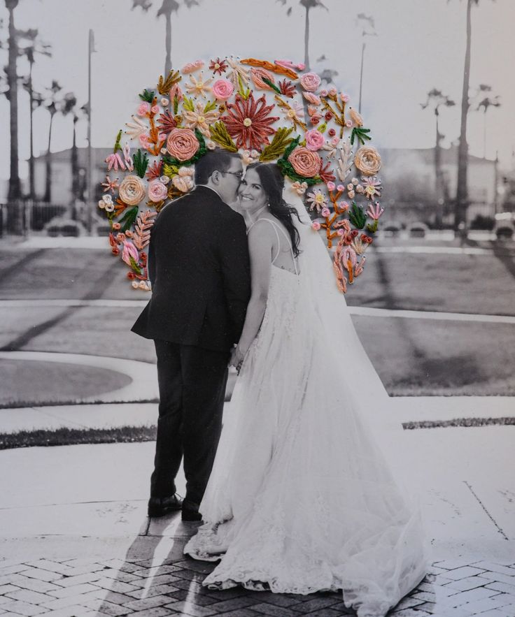 a bride and groom are standing under an umbrella with flowers on the head, in front of palm trees