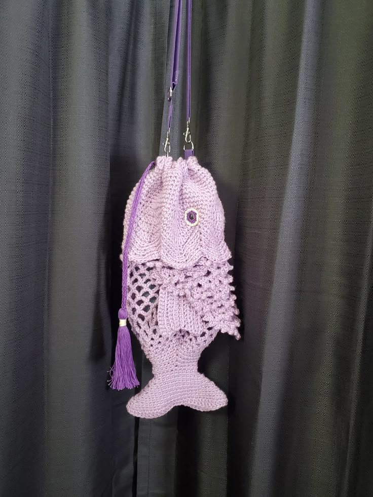 a crocheted purse hanging on a curtain with a purple tasselled handle