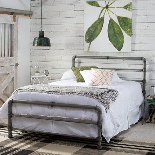 a bedroom with white brick walls and wood floors, an iron bed frame is in the foreground