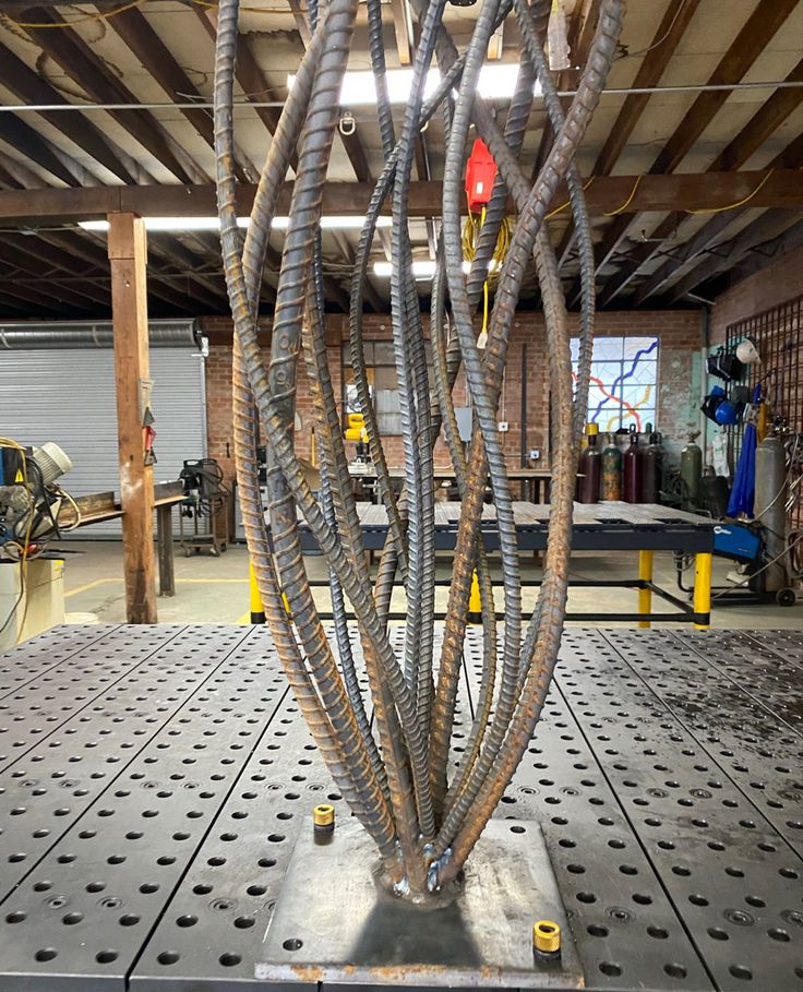 a metal structure with many wires attached to it in a warehouse or workshop, surrounded by tools and machinery