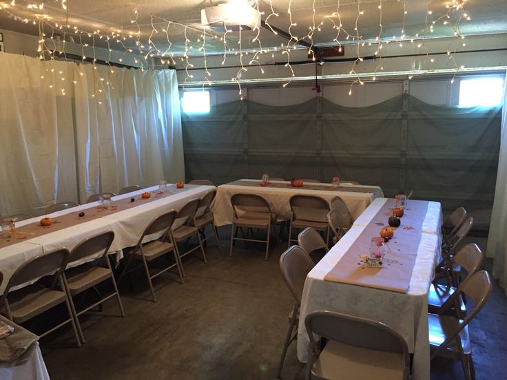 a room filled with lots of tables covered in white tablecloths and lights hanging from the ceiling