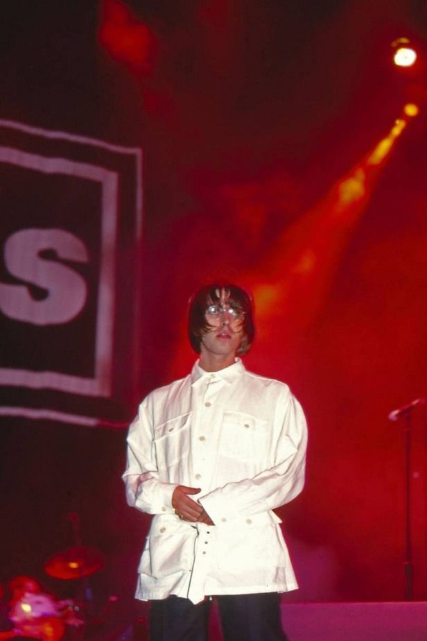 a man standing in front of a microphone on stage with his hands folded out and wearing a white jacket