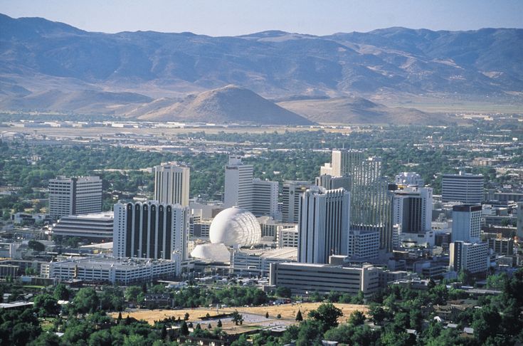 an aerial view of a city with mountains in the background and trees on the foreground