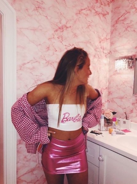 a woman standing in front of a bathroom mirror wearing a pink skirt and crop top