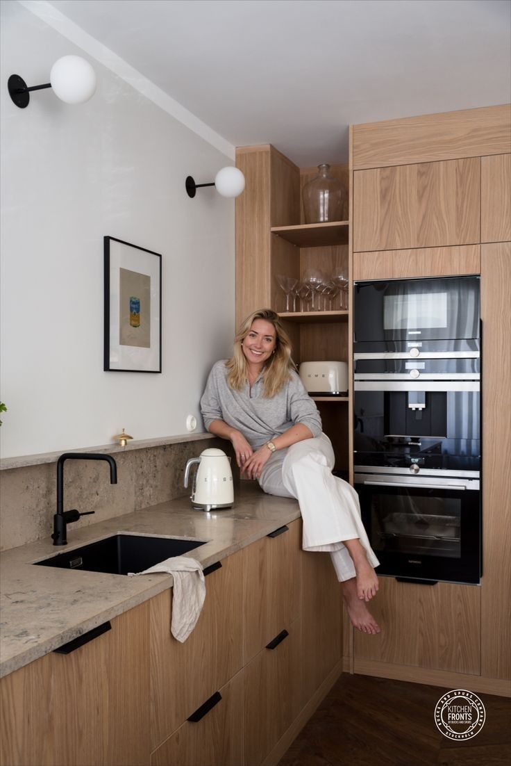 a woman sitting on top of a kitchen counter next to a sink and oven in a room